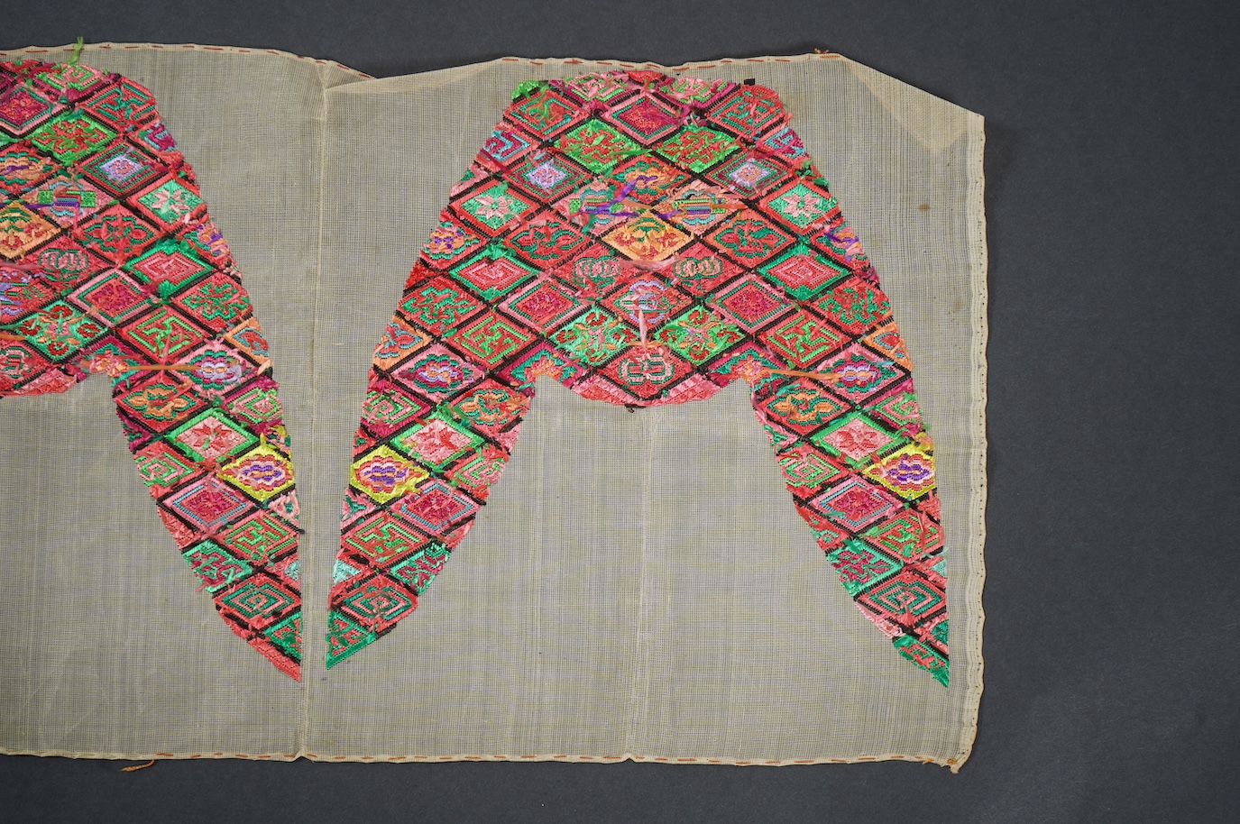 A pair of early 20th century Chinese silk polychrome finely embroidered slipper fronts, possibly from Guangxi province. Embroidered in a diamond grid, with stylistic and symbolic motifs. 21.5cm top to base. Condition - u